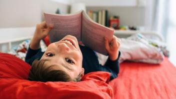 Young boy reading a book on his bed