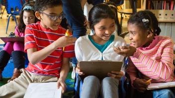 Three elementary students laughing and talking bout a project in their classroom