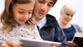 Young child looking at tablet with her father