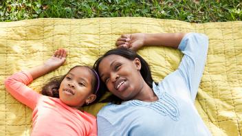 Mother and young daughter lying on blanket outside and talking