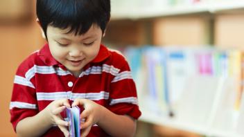 preschool boy looking at book in library