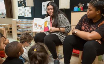 two preschool teachers doing a read aloud for a group of young kids